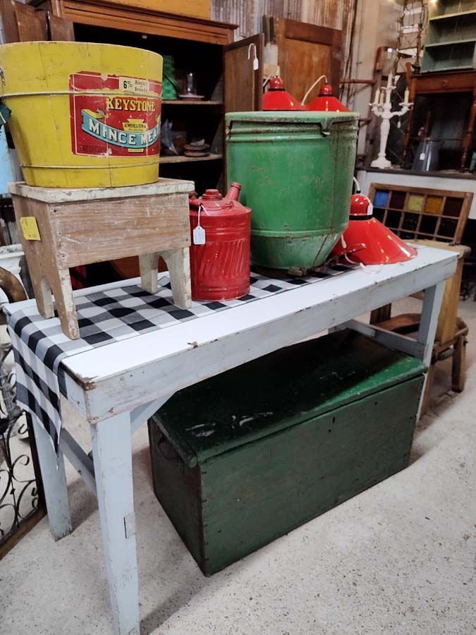 Antique store display: yellow bucket, green bin, red lamps, table, and trunk.