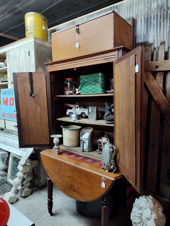 An antique cabinet with open doors, displaying items inside, with a drop-leaf table in front.