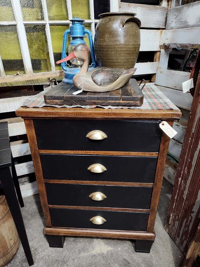 Black and brown wooden nightstand with brass handles. Top is holding a duck statue and pottery.