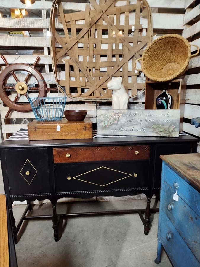 Antique black buffet table with decorative trim and various decor: basket, art, and a blue dresser.