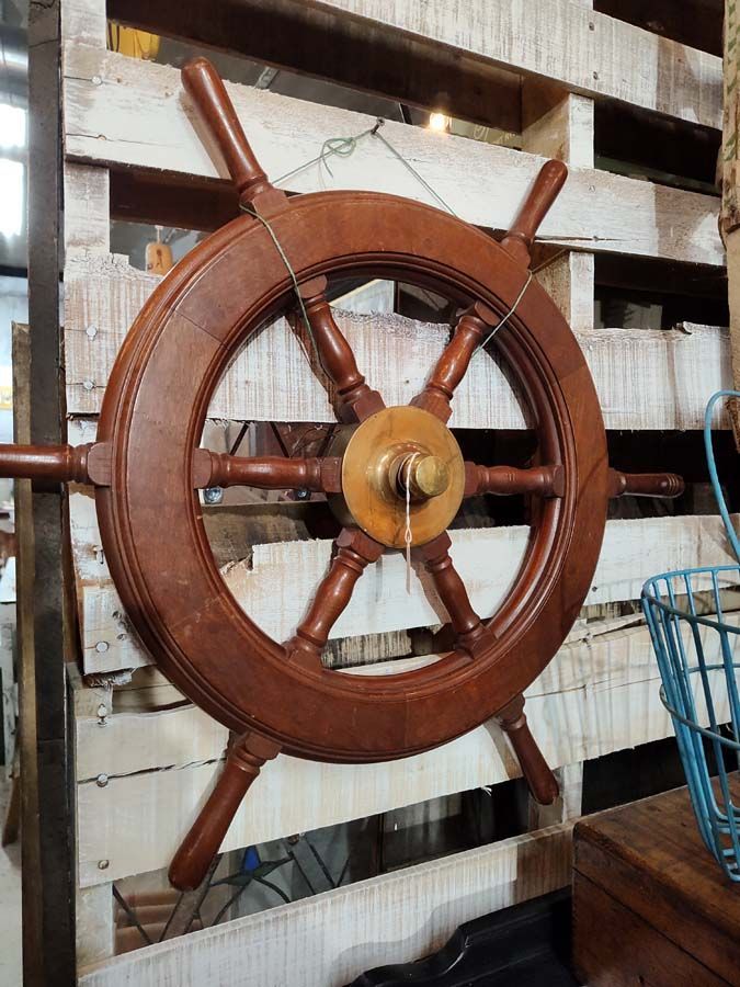 Wooden ship's wheel with brass center, mounted on a white pallet.