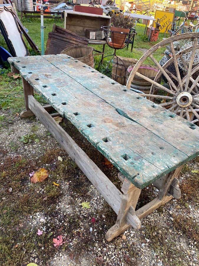 Weathered wooden work table with teal paint, outdoors near a wagon wheel and other yard items.