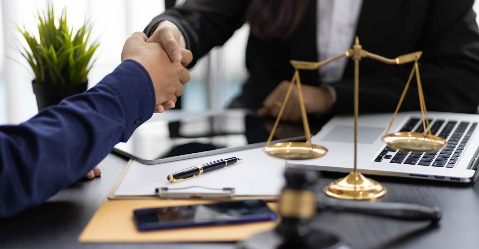 A man and a woman are shaking hands in front of a scale of justice.