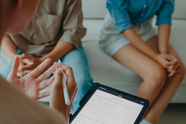 A woman is holding a pen and a tablet while talking to a couple.