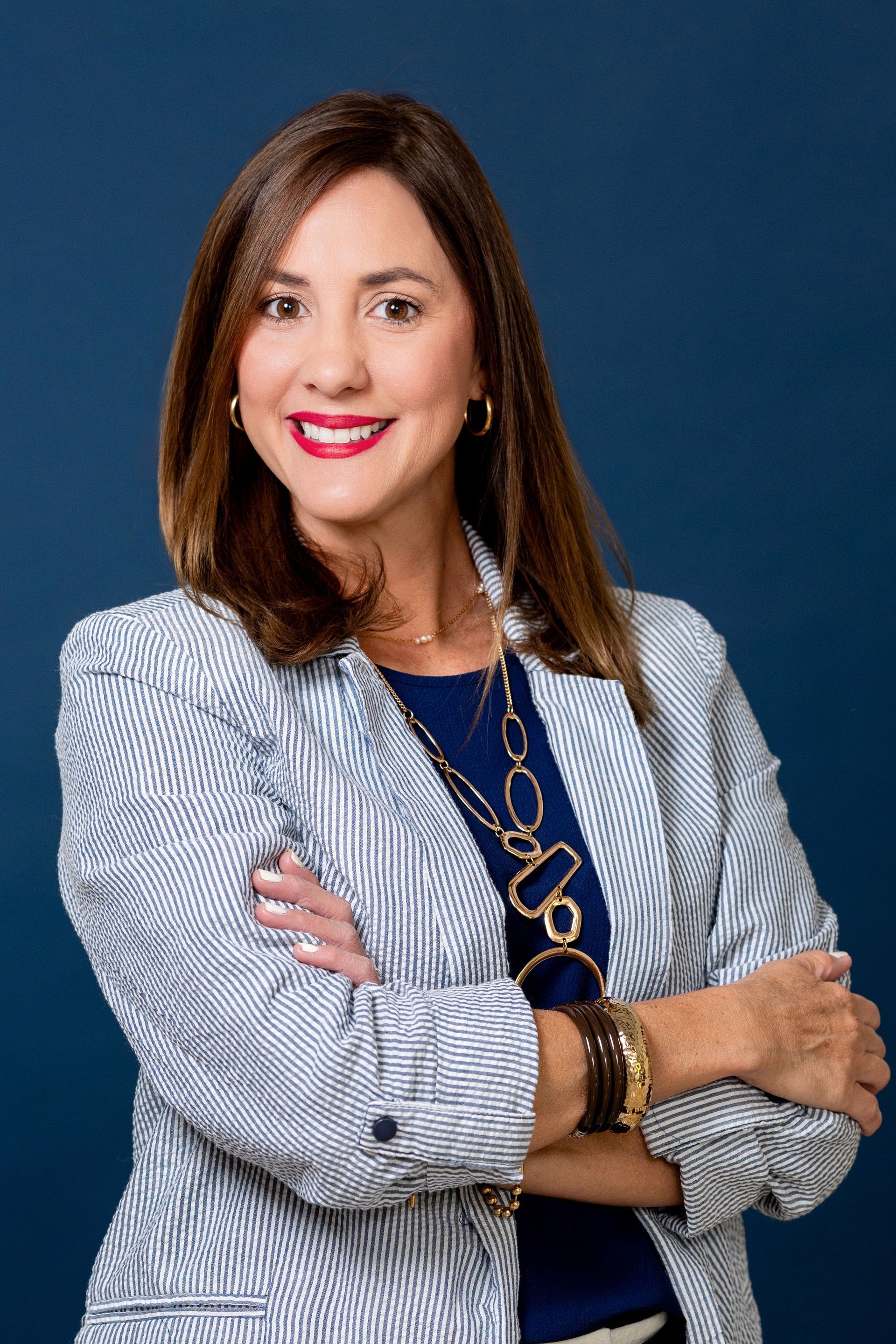 Larissa Rivera in a blue patterned blazer, smiling with arms crossed against a dark blue background