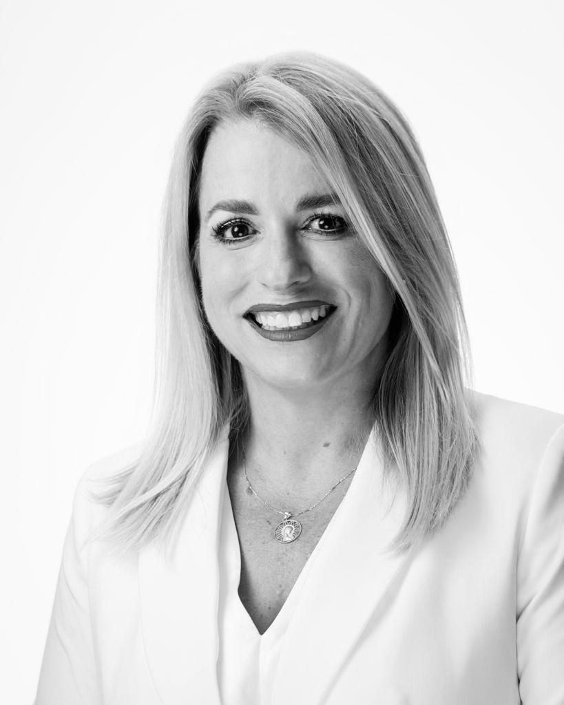 Marie Frances smiles, wearing a white blazer and necklace, posing against a white background.