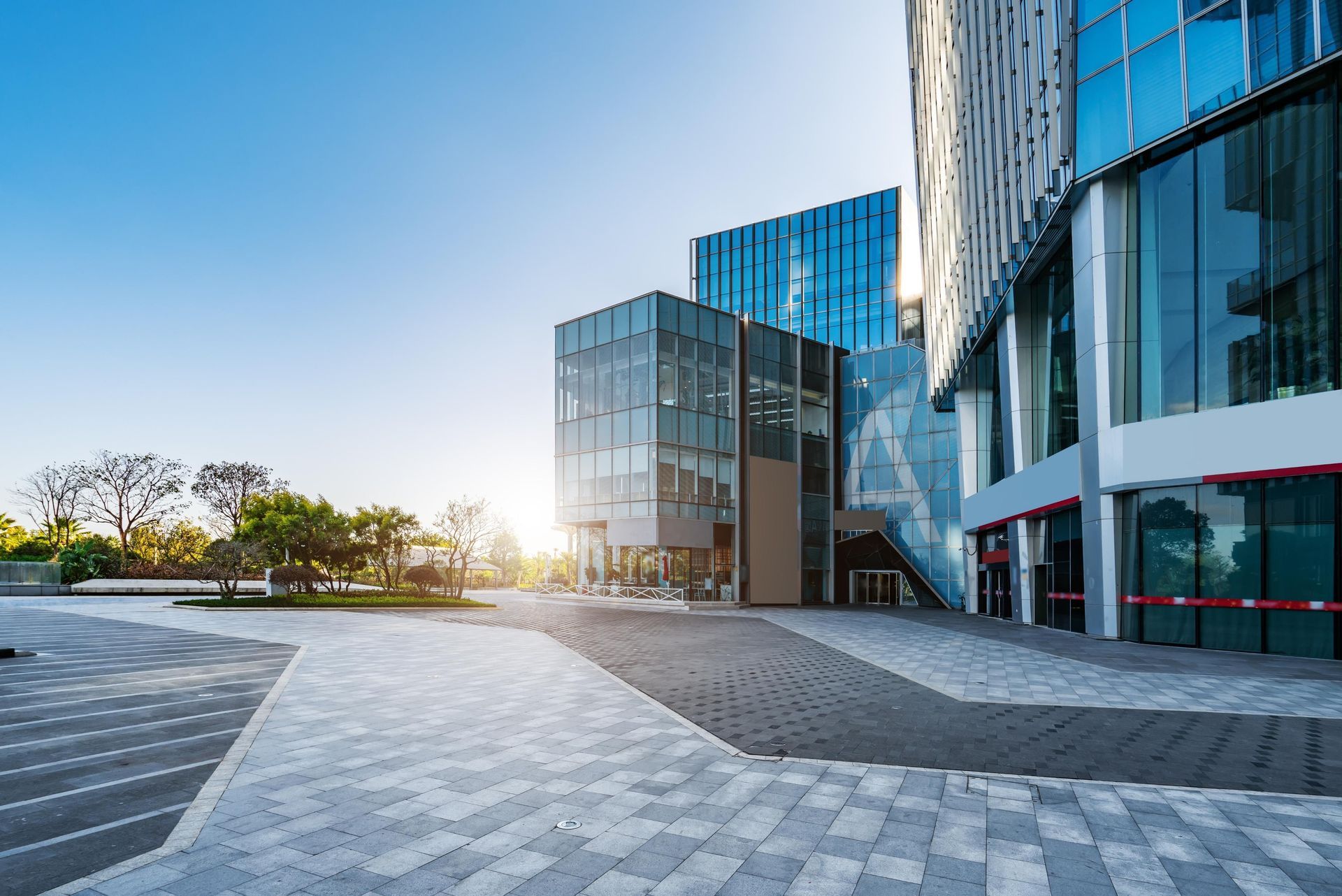 Modern glass building with paved walkways and sunny sky.