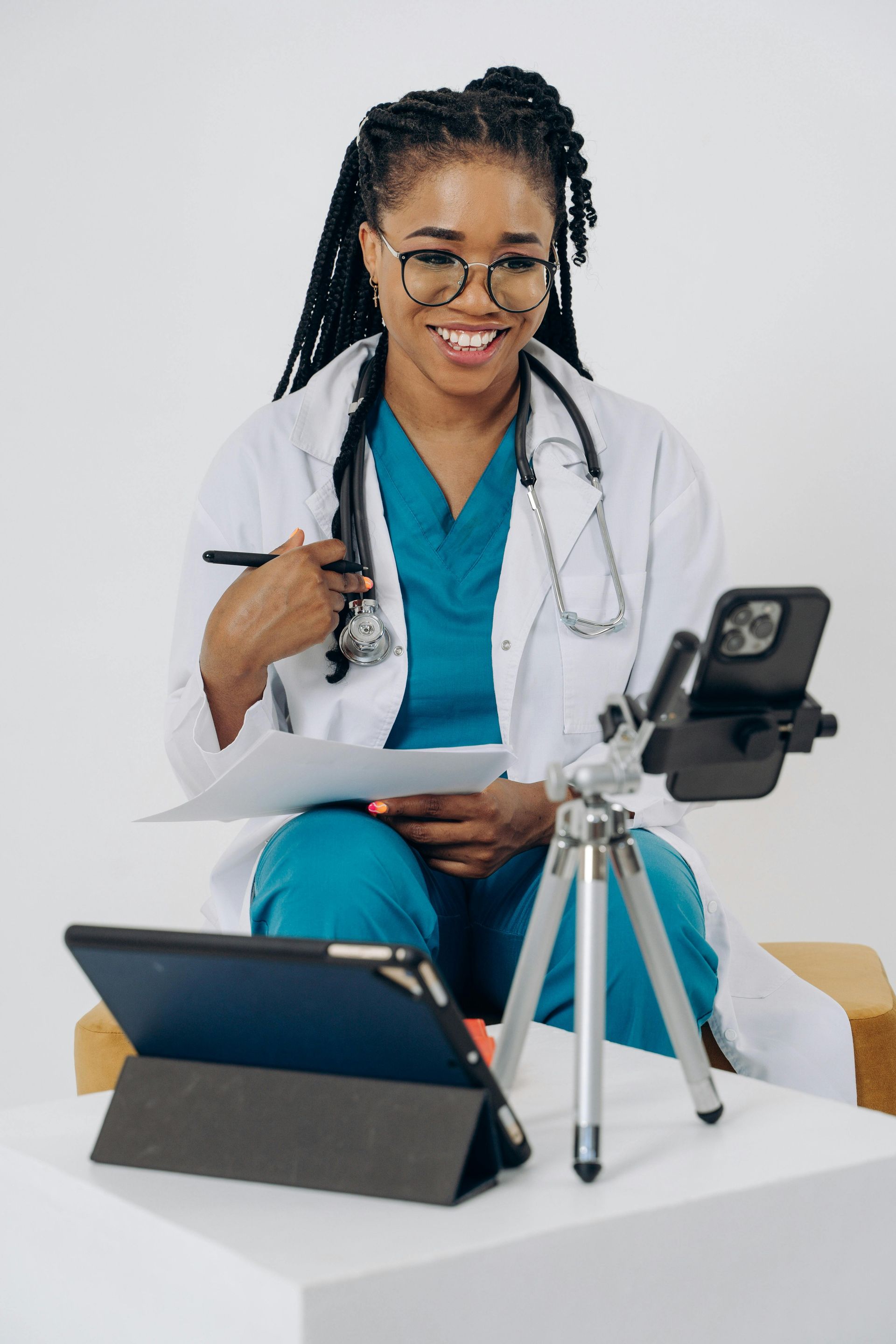Doctor in blue scrubs and white coat using tablet and smartphone for telemedicine.