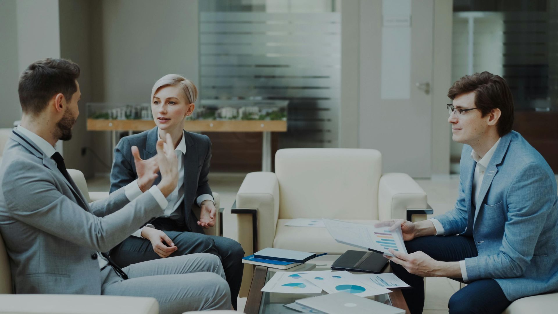 Three people in a business meeting, discussing documents in a bright office lounge.
