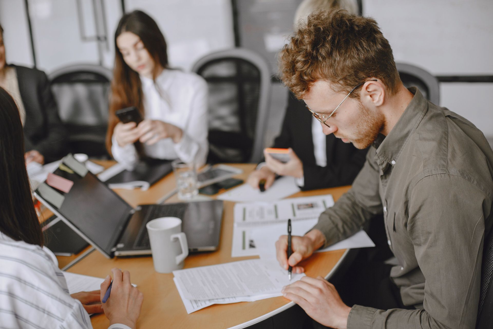 People in a meeting room working at a table with laptops, papers, and notebooks