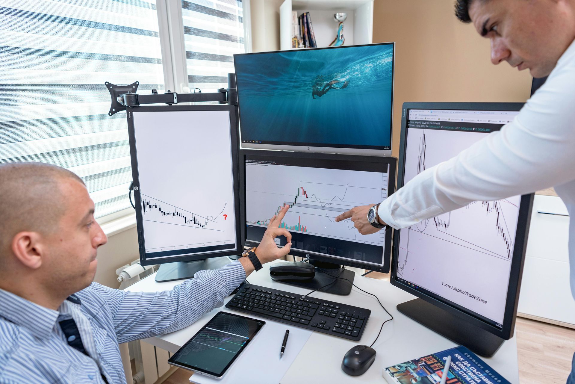 Two men analyzing stock charts on multiple computer monitors in an office setting.