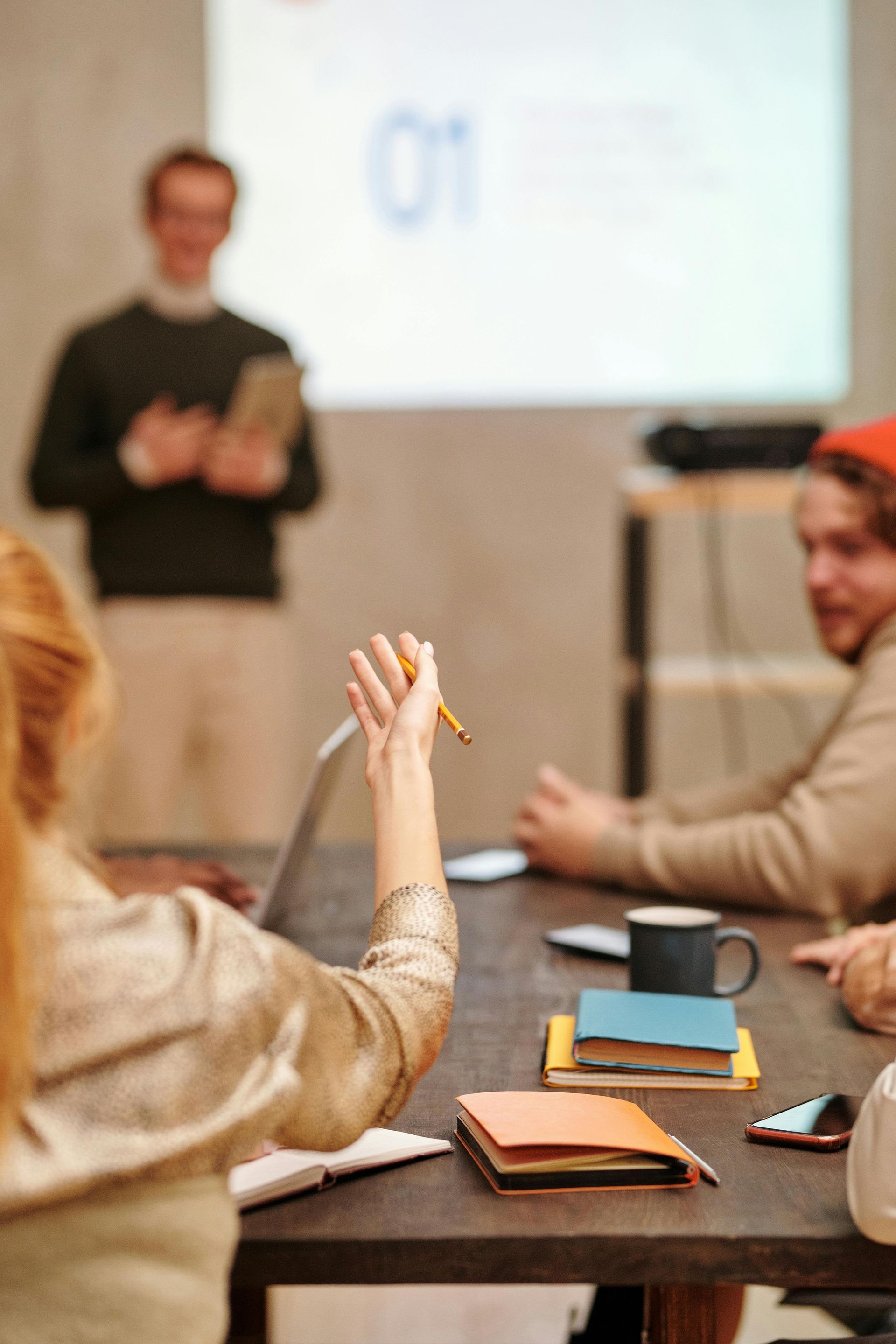 Meeting room with presenter at screen and attendees around a table taking notes
