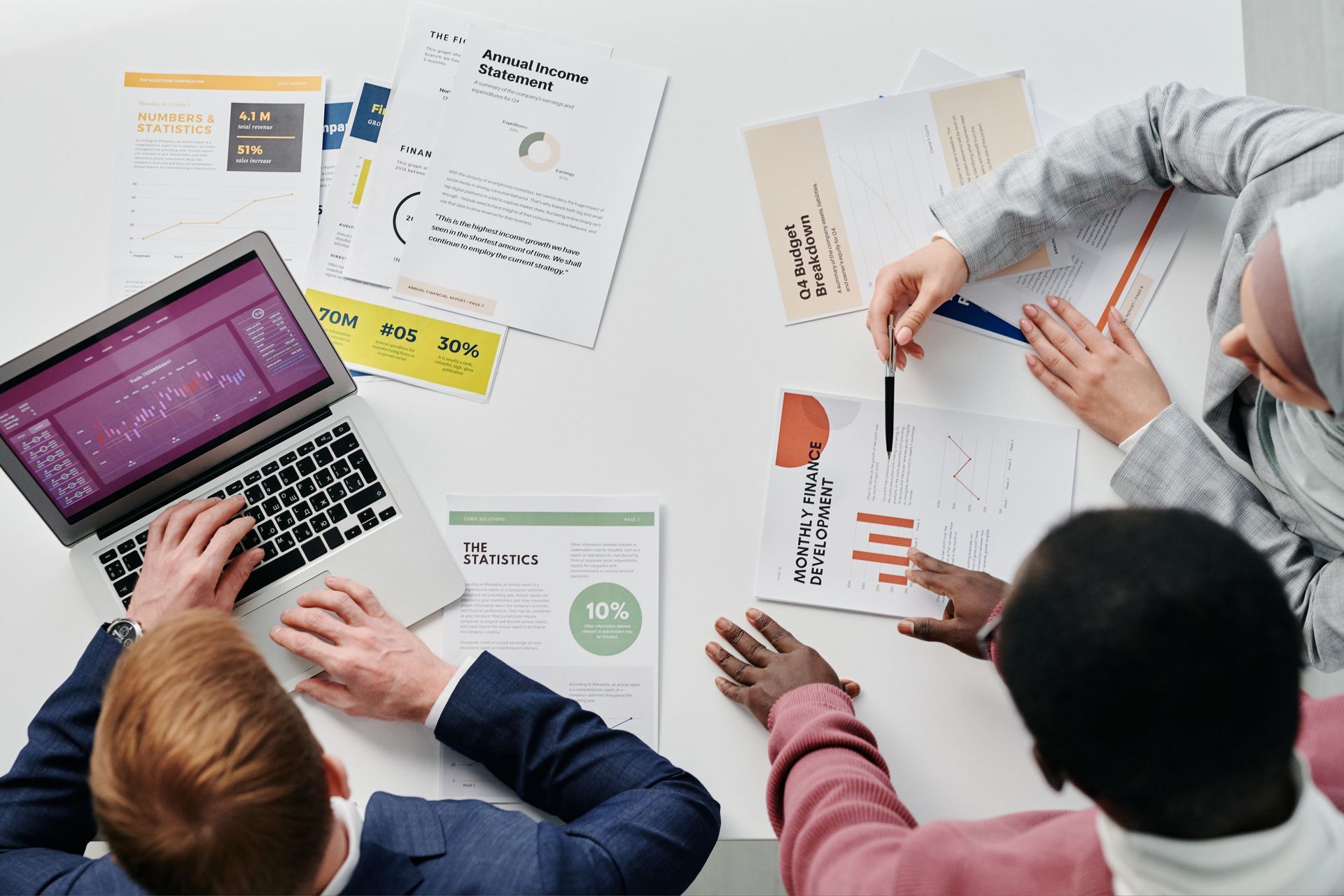 Team reviewing charts and laptops around a meeting table with documents and hand gestures