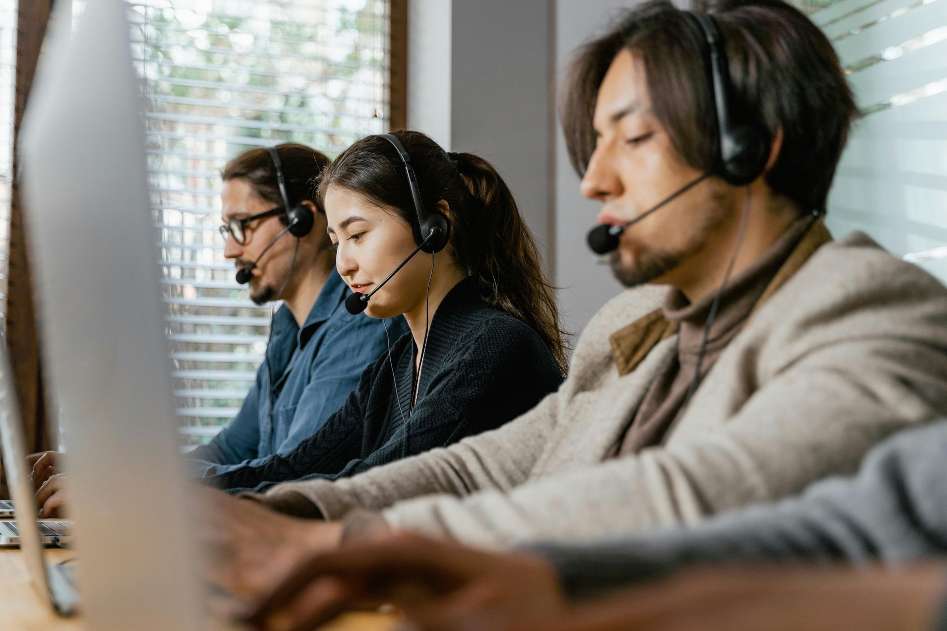 Three people wearing headsets and working on computers in an office setting.