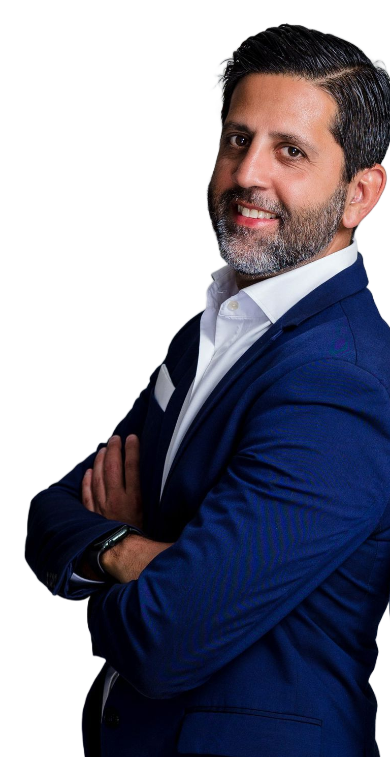 A person with a beard and dark hair wearing a blue blazer and white shirt, smiling with arms crossed against a white background.