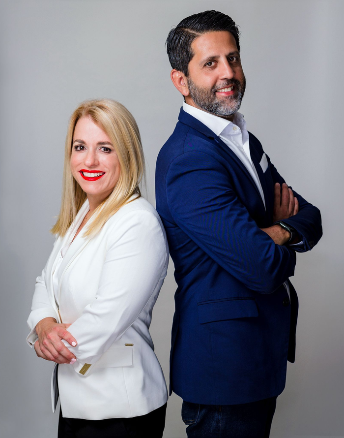 José Arroyo y Marie Frances López, back-to-back, smiling. Formal wear on a white background.