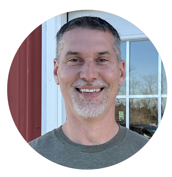 A man with a beard is smiling in front of a window