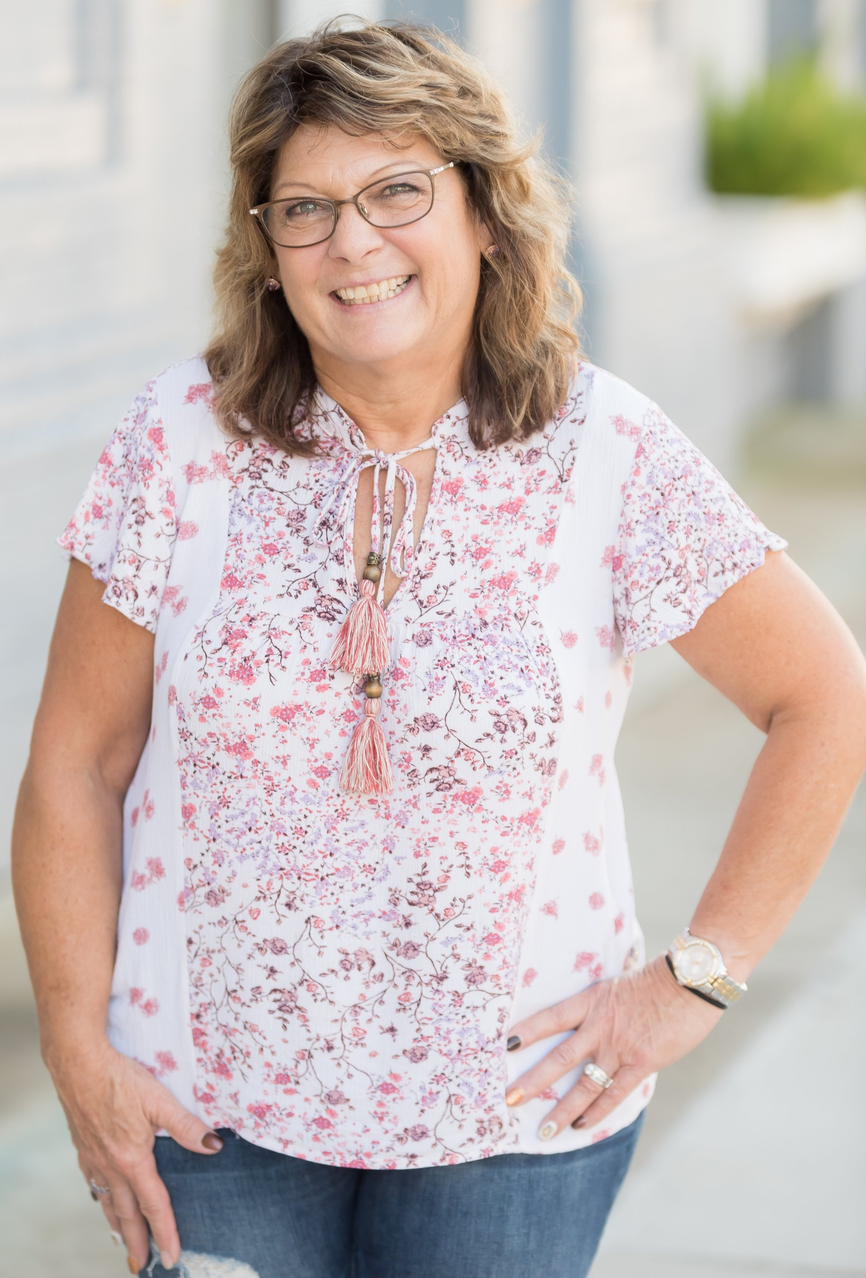 A woman wearing glasses and a blue shirt is smiling for the camera.