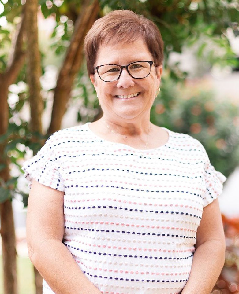 A woman wearing glasses and a striped shirt is smiling in front of a wooden wall.
