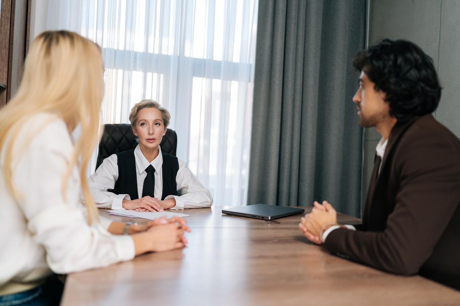 Three people at a table in an office setting. Two clients face a woman in a suit.