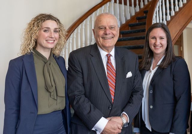 Hands stacked together in a team huddle over a wooden table with notebooks and a pencil.