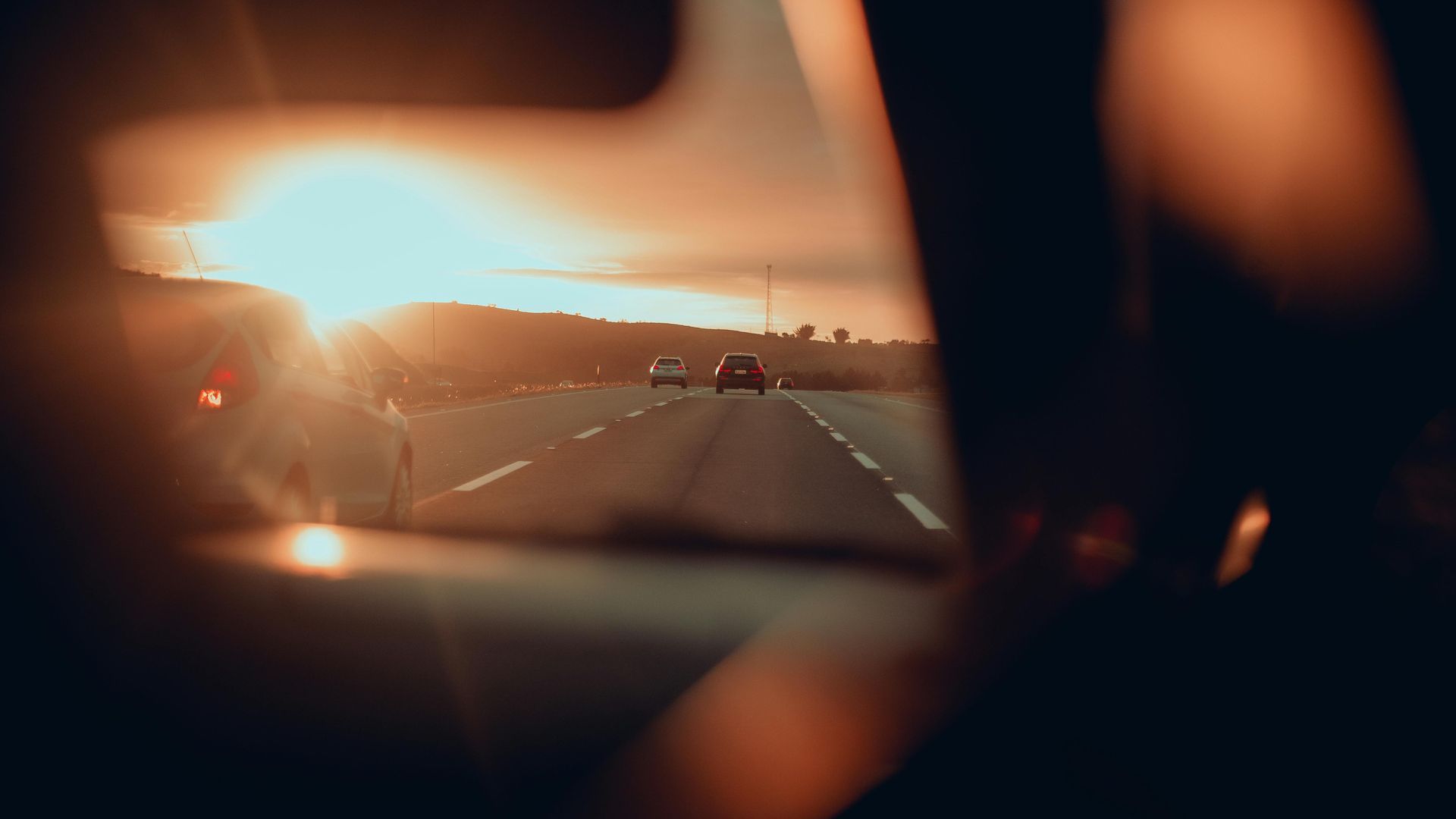 Sunset view from a car's interior, over a highway. Orange sky, other cars on the road.
