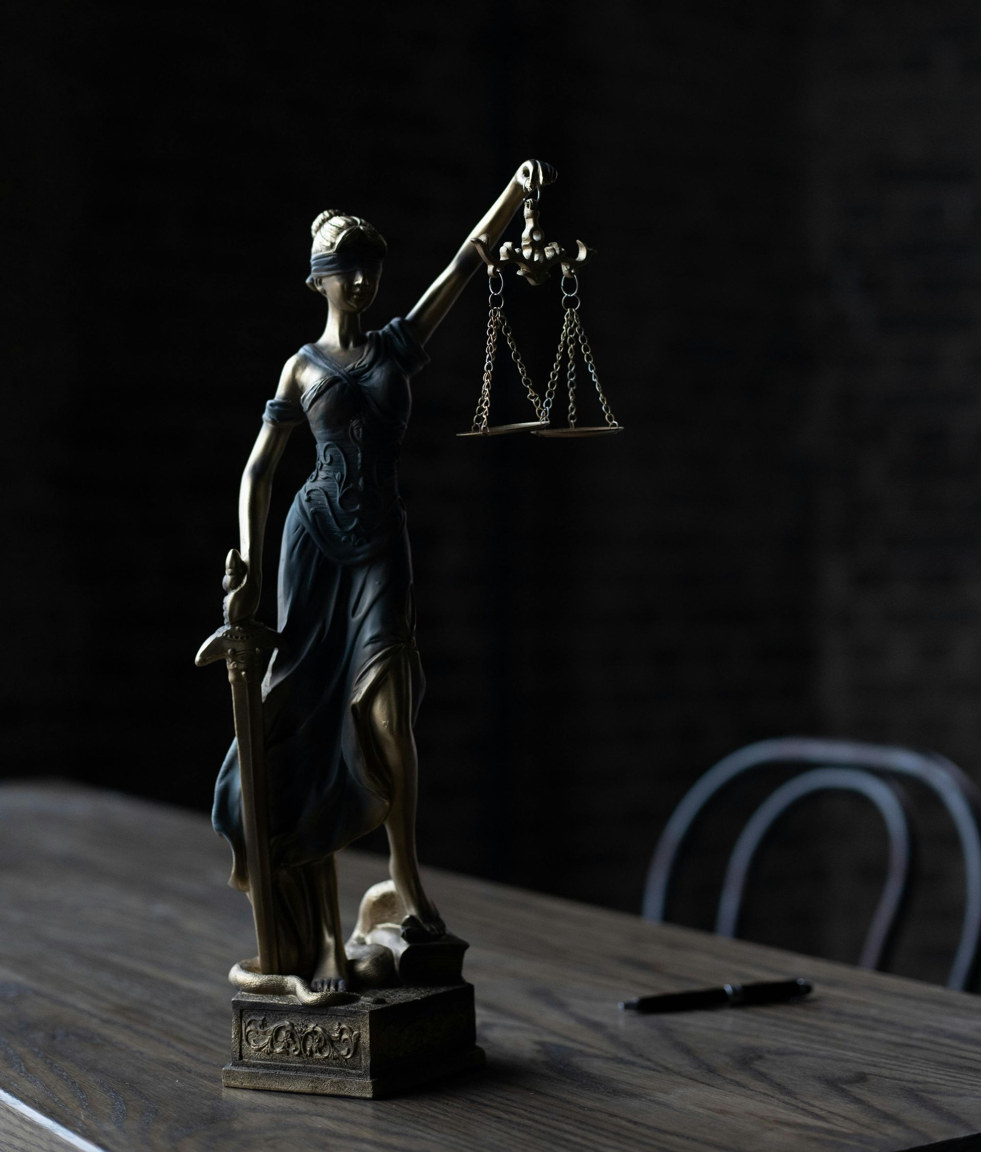 Statue of Lady Justice on a wooden table, holding scales, in a dimly lit room.