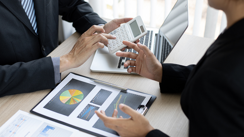 A man and a woman are sitting at a table with a laptop and a calculator.