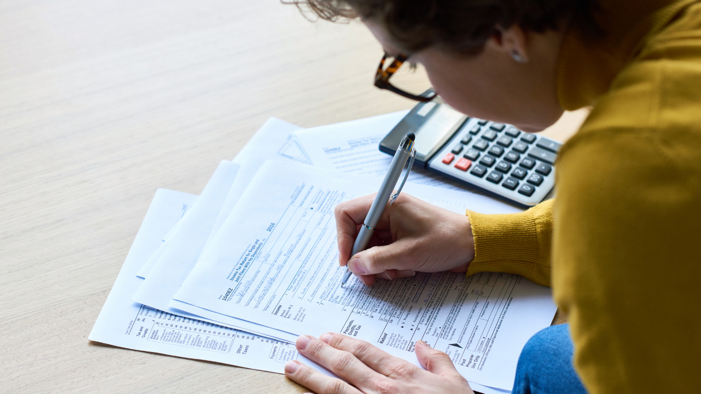 A woman is sitting on the floor writing on a piece of paper next to a calculator.