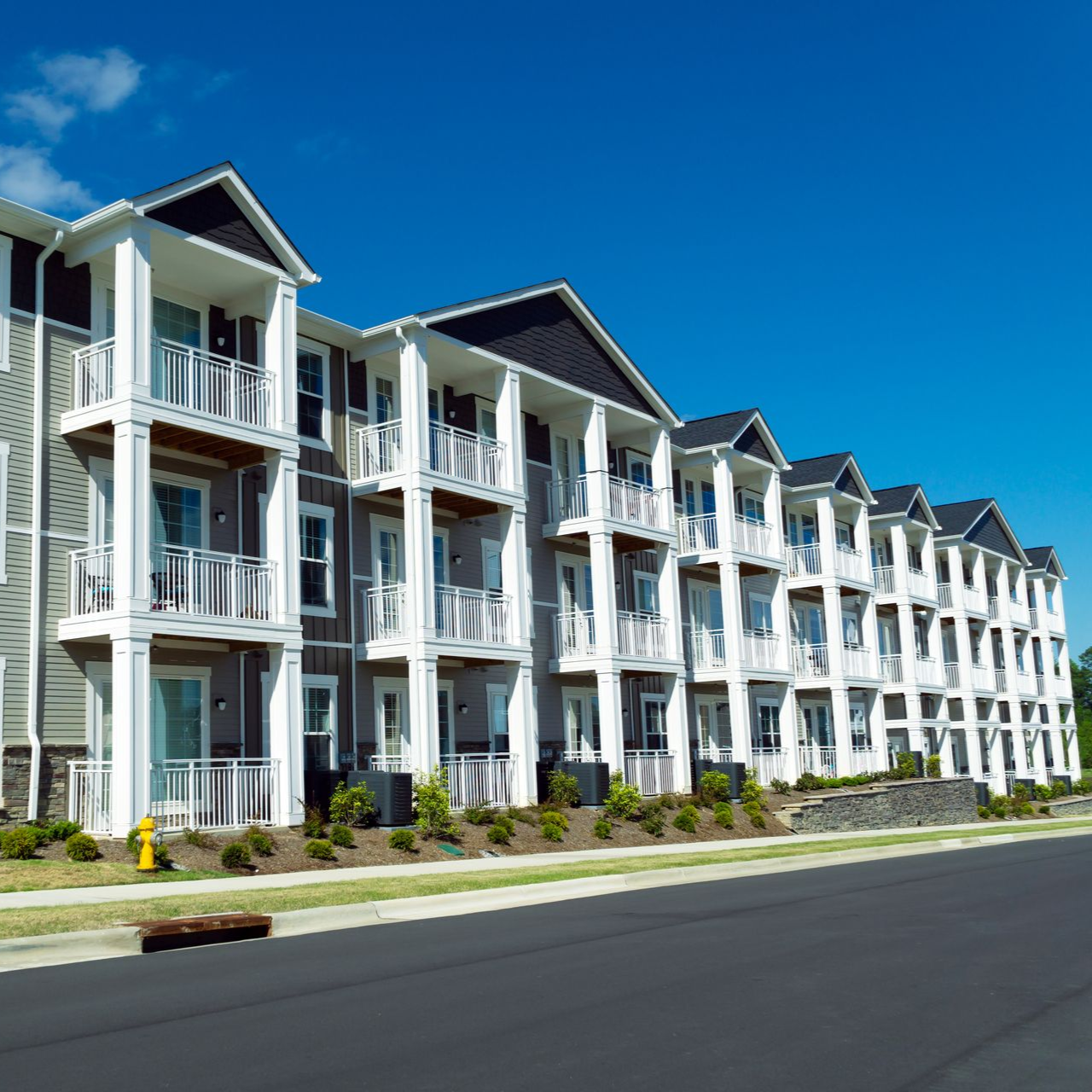 Multi-story apartment building with gray siding, white trim, balconies, and blue sky.