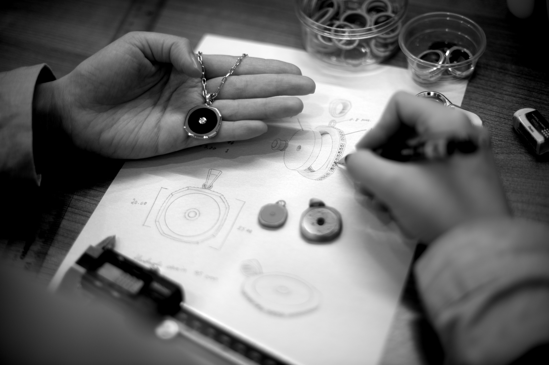Ein Schwarzweißfoto einer Person, die eine Designskizze einer Halskette zeichnet.