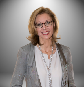 Eine Frau mit Brille und Halskette lächelt in die Kamera