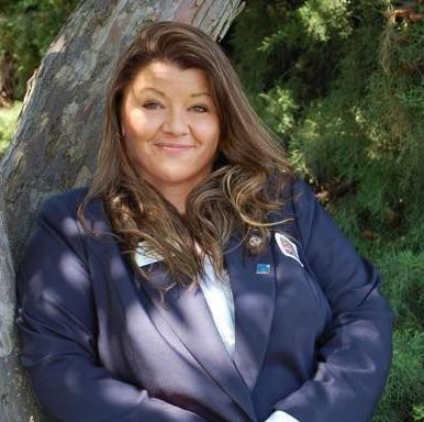 A woman in a suit is leaning against a tree and smiling.