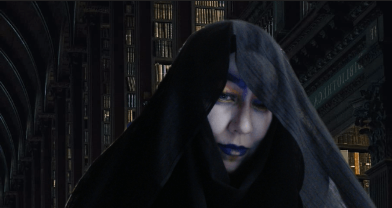 A woman with blue paint on her face is wearing a black veil over her head, representing Destiny.