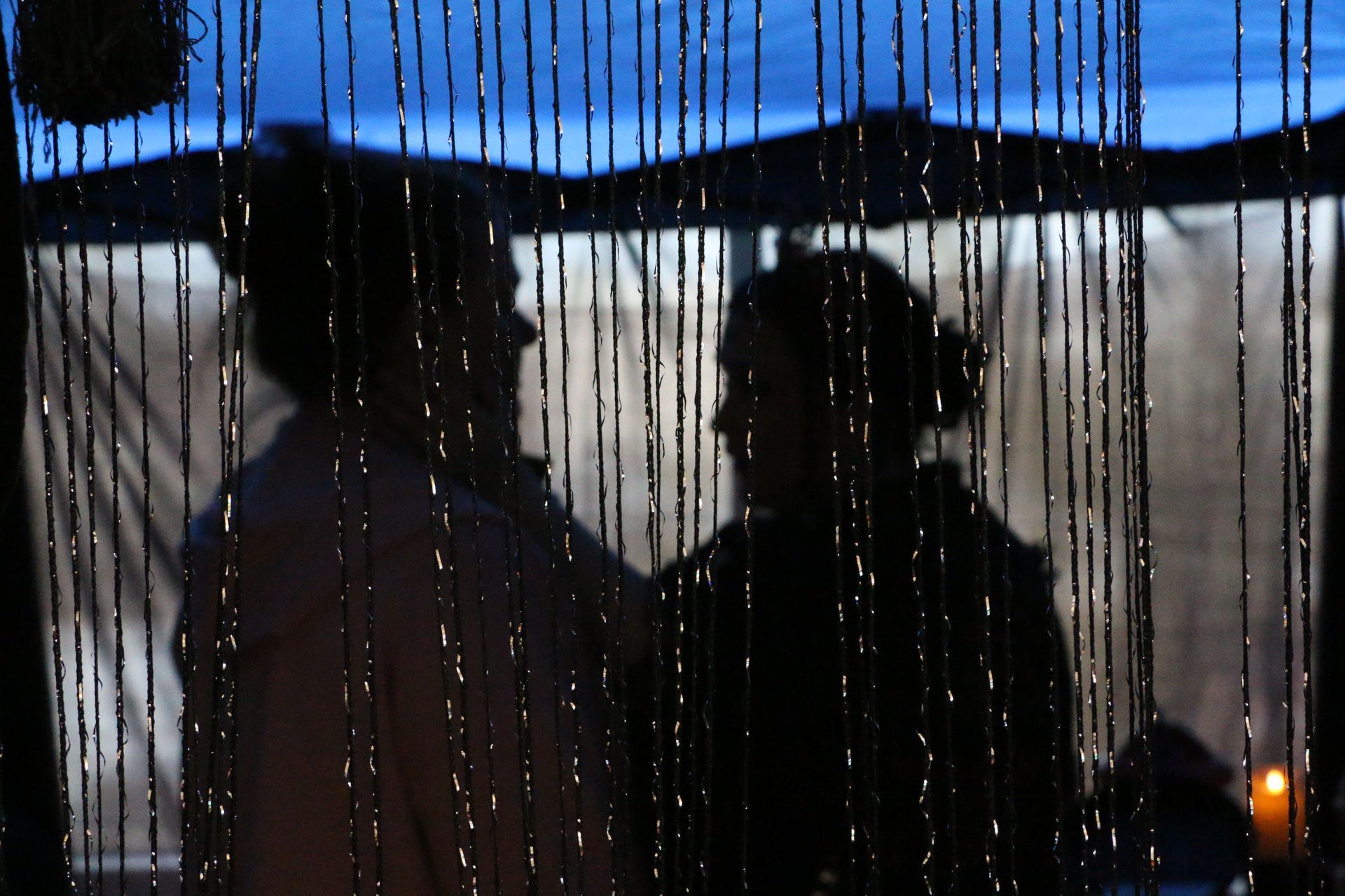 A man and a woman are standing in front of a beaded curtain.