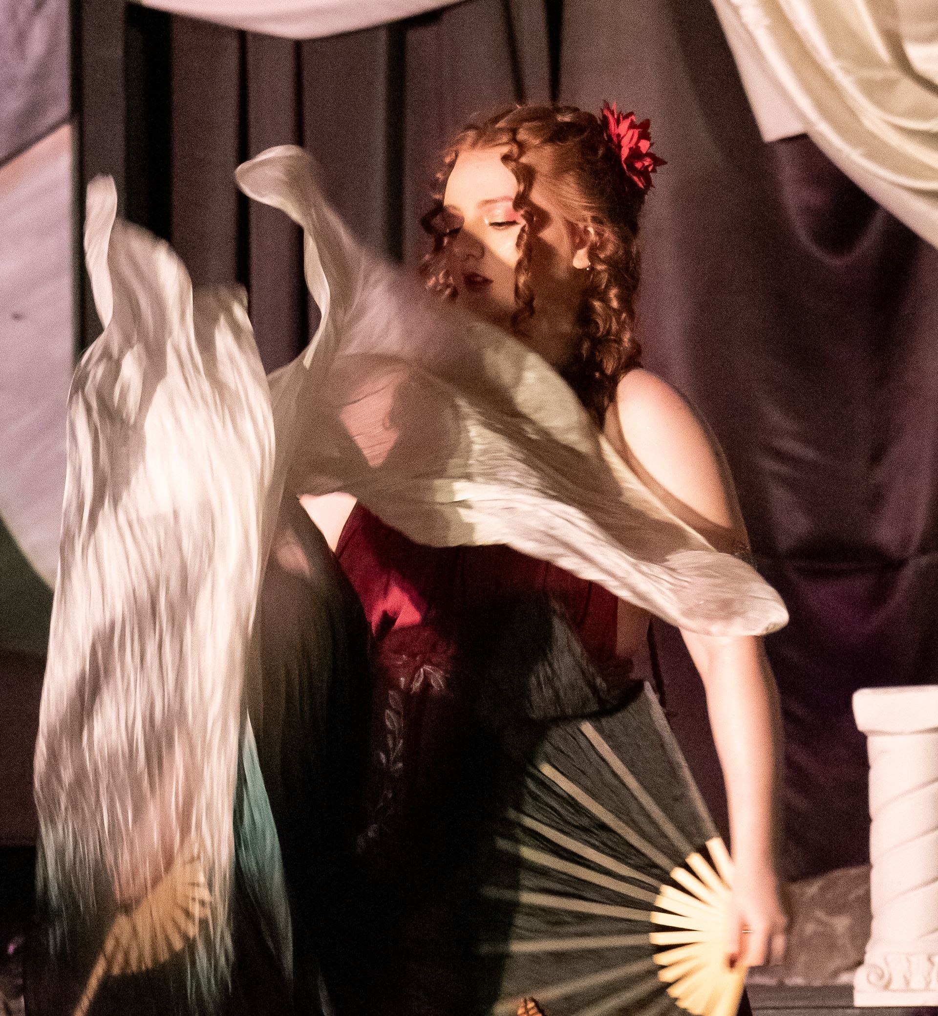 A woman in a black dress is standing in front of a gold curtain.