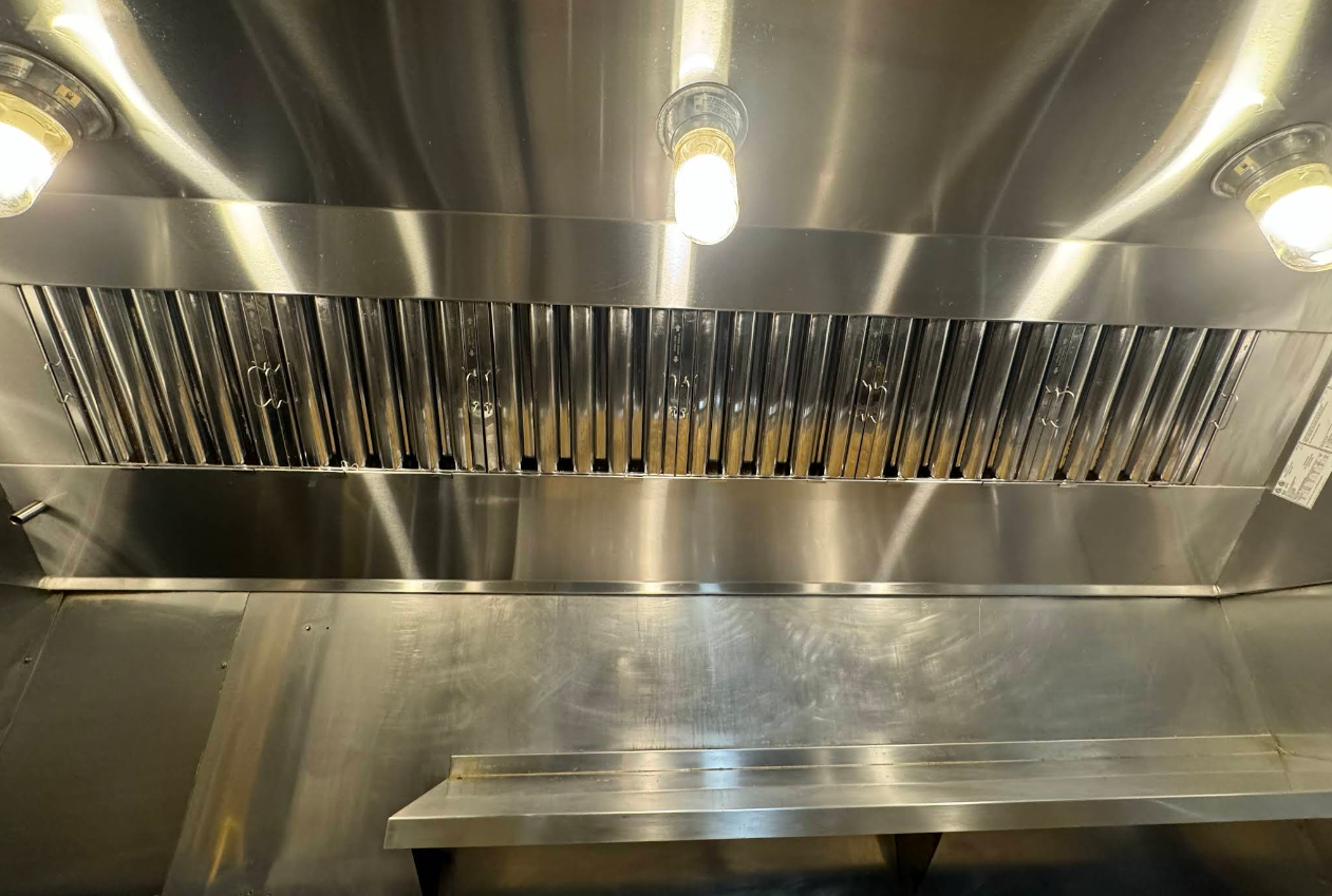 Stainless steel commercial kitchen range hood with lights and filter.