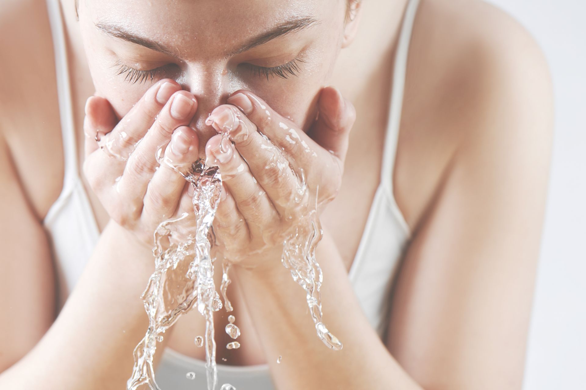 A woman is washing her face with water from her hands.