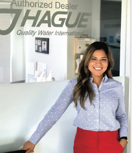 Norma Lara smiling in front of a window that says Hague Quality Water