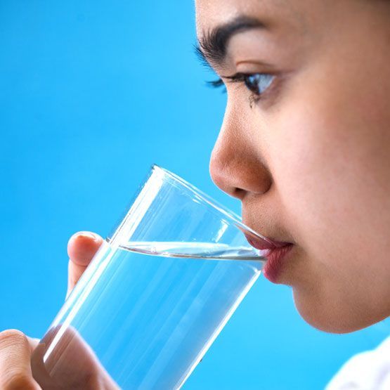 a woman is drinking a glass of water on a blue background .