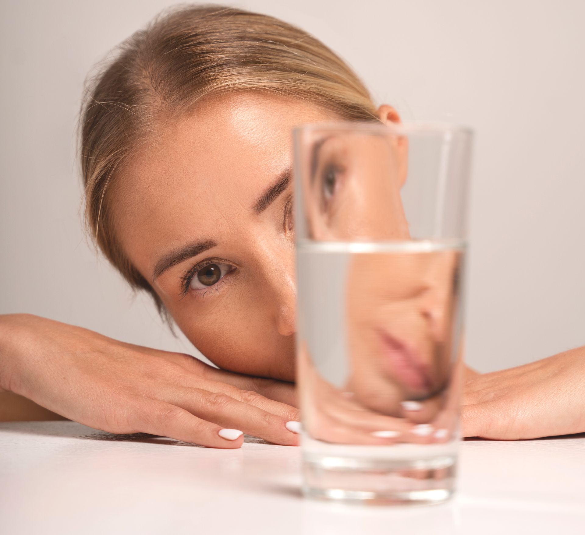 woman looks questionably through a glass of water on a table