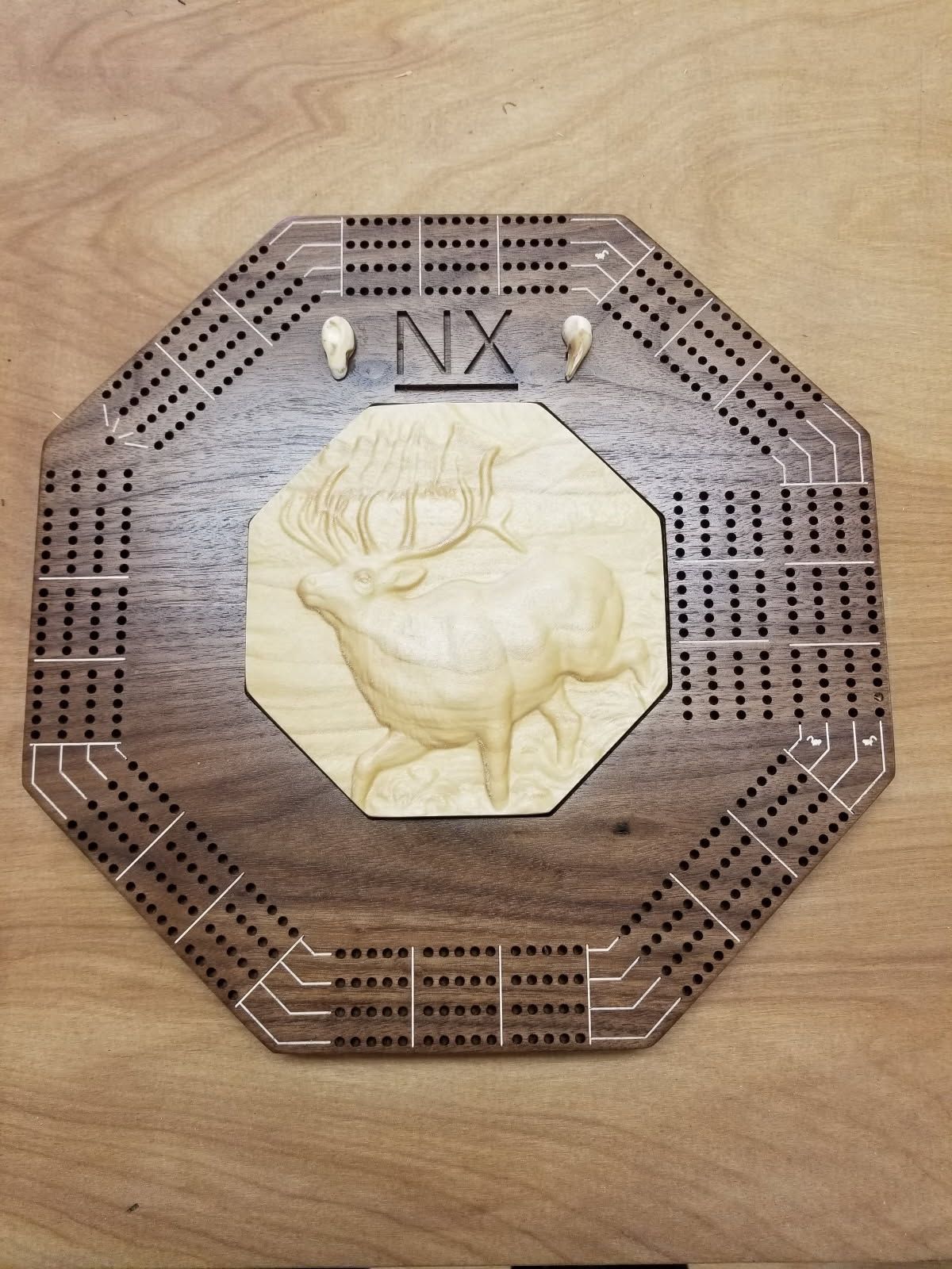 A wooden cribbage board with a deer on it is sitting on a wooden table.