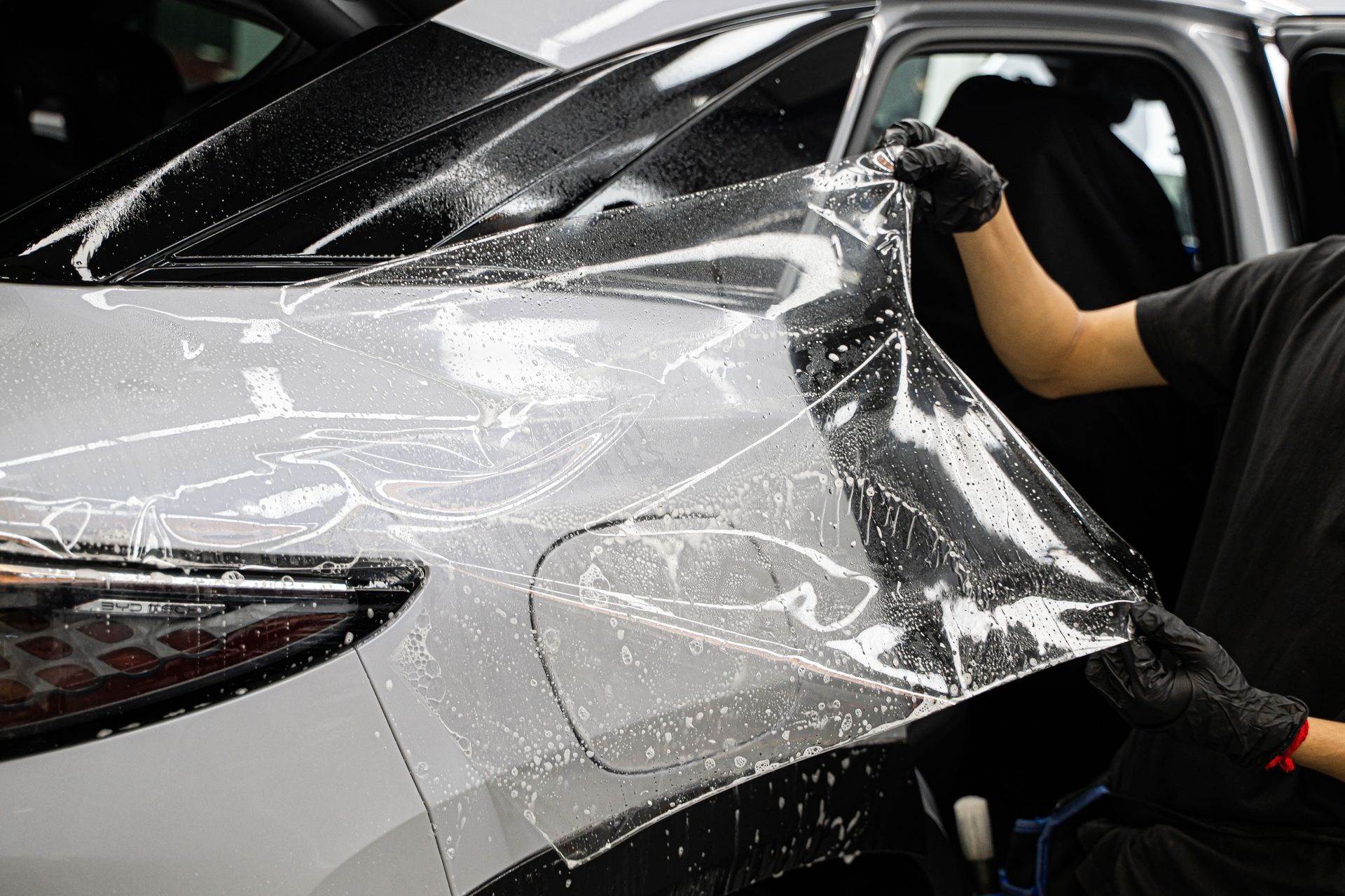 People viewing cars in a garage; some cars are on lifts, others are on the floor.