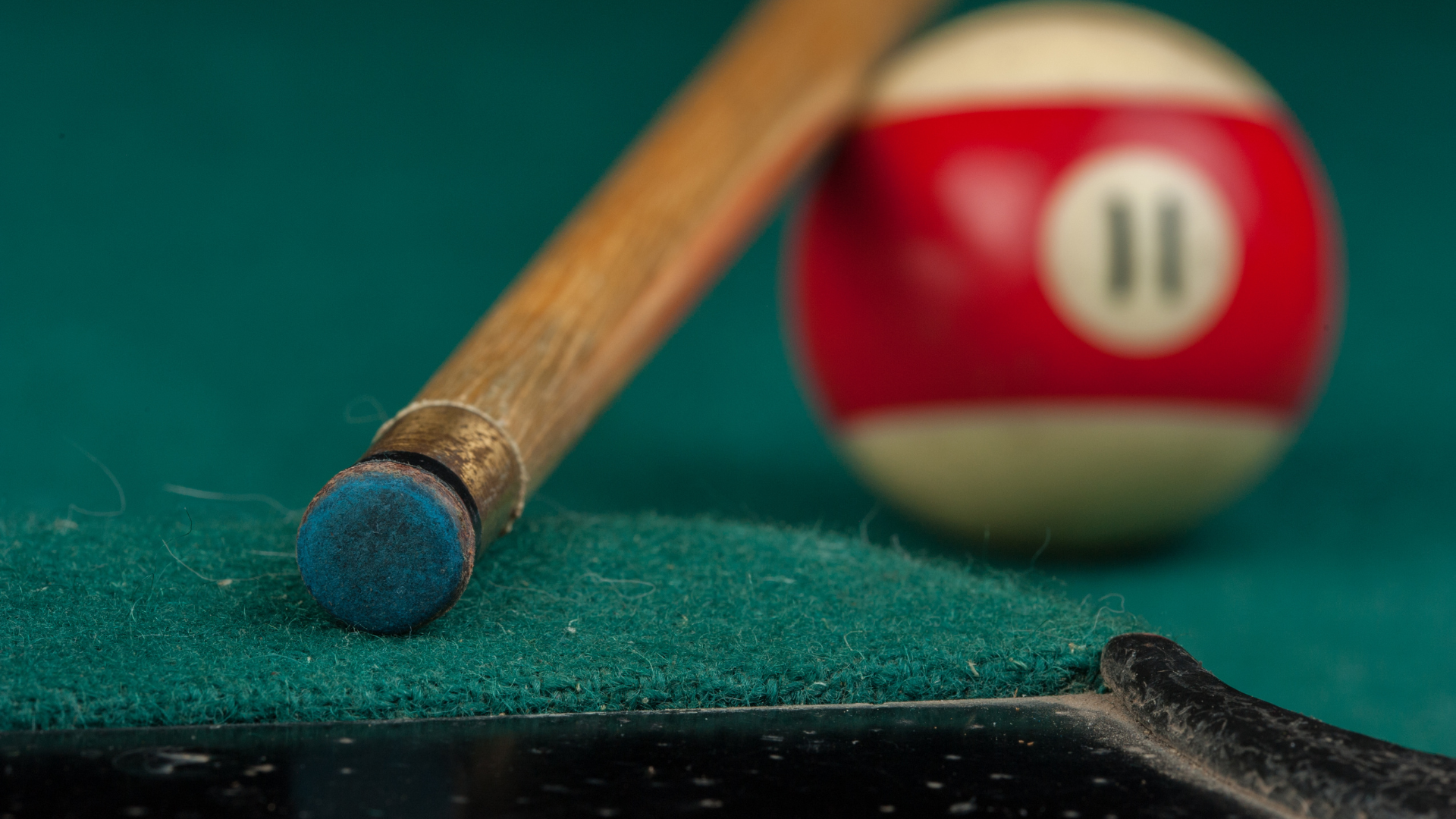 Pool cue and red 11 ball resting on a green felt pool table.