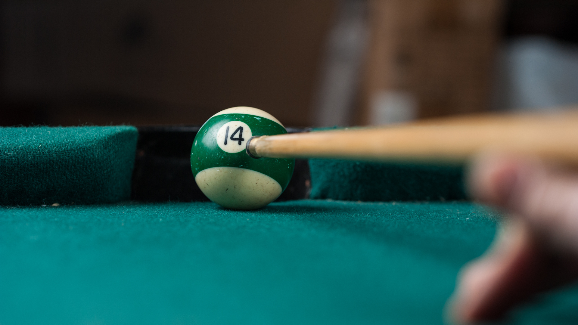 Pool cue about to strike the green 14-ball on a pool table.