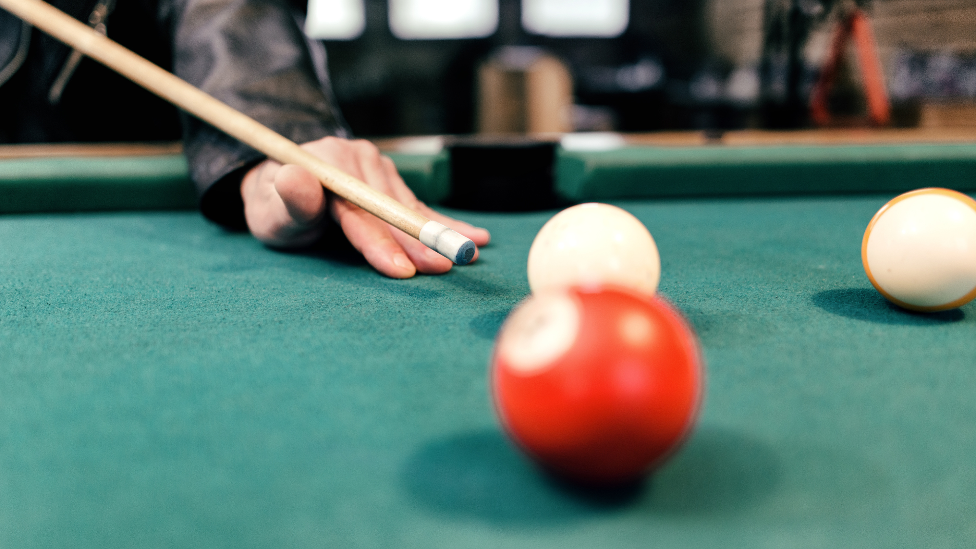 Person about to strike a white cue ball with a pool cue; other balls are visible on a green felt table.