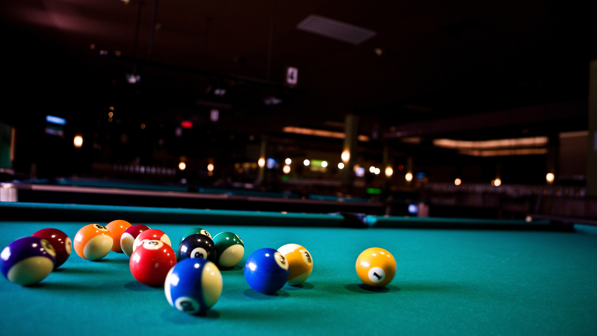 Pool balls scattered on a green felt table in a dimly lit pool hall.