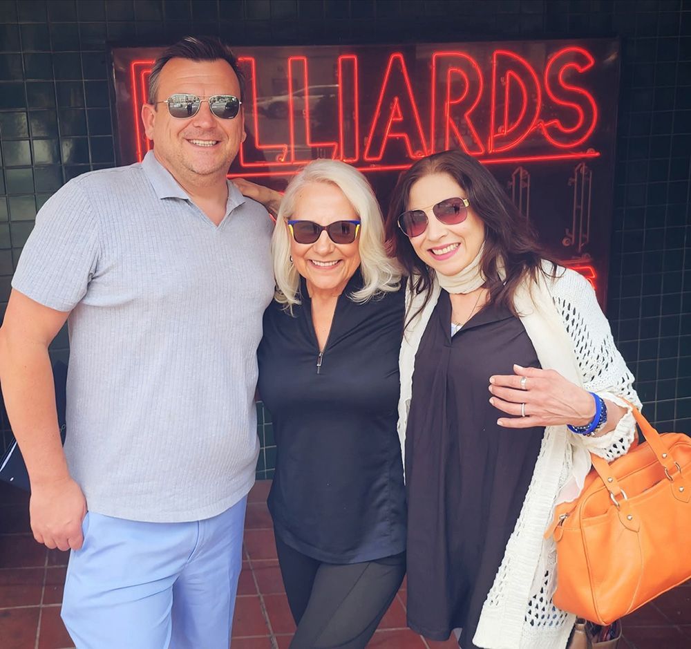 Three people smiling in front of a neon 