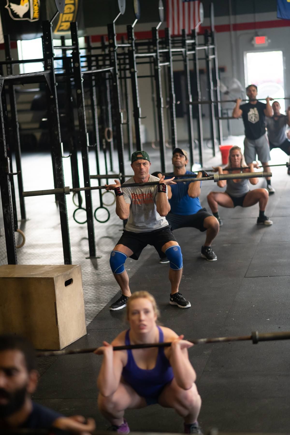 A group of people are squatting with barbells in a gym.