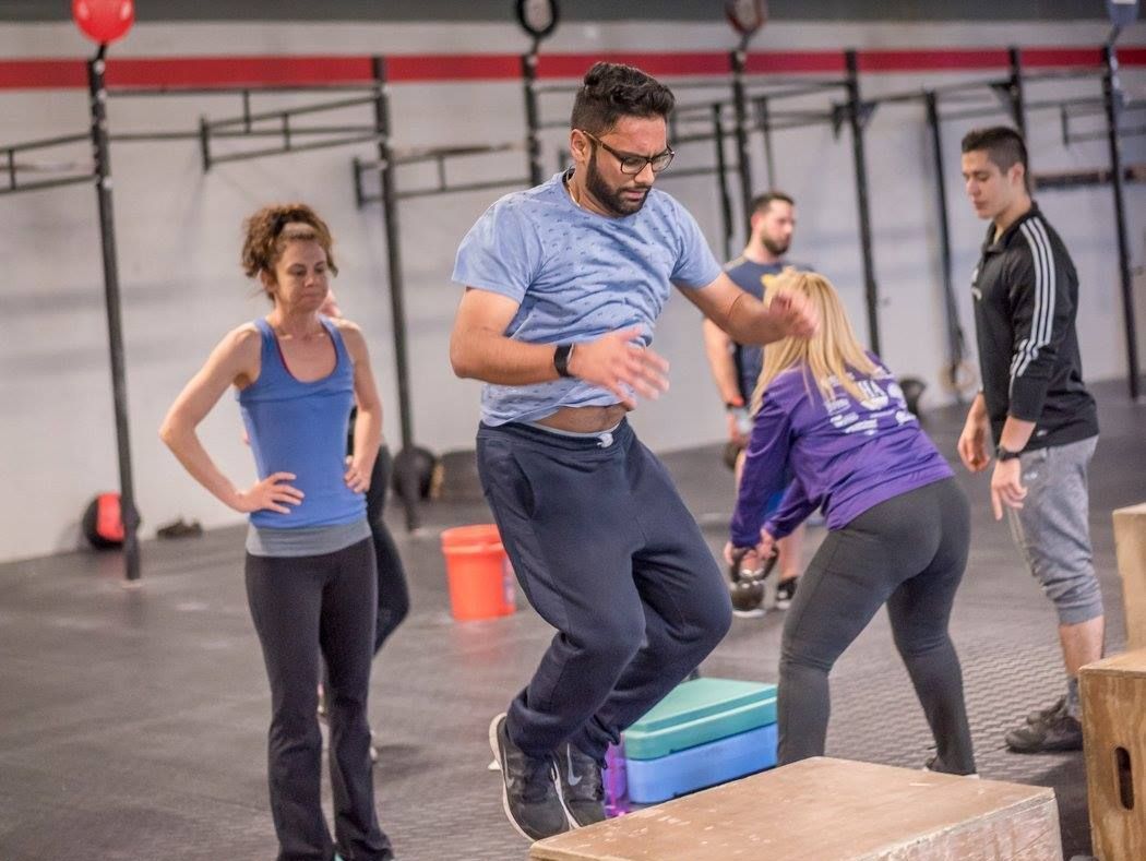 A man is jumping over a box in a gym while a woman watches.